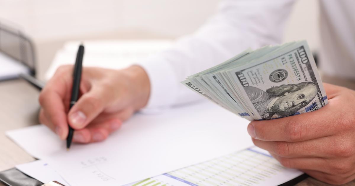 Finance professional handing over cash for a business expense while writing on a financial report